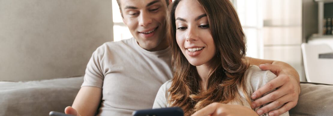 young couple relaxing together on their sofa playing Jackpot Capital games on their phones