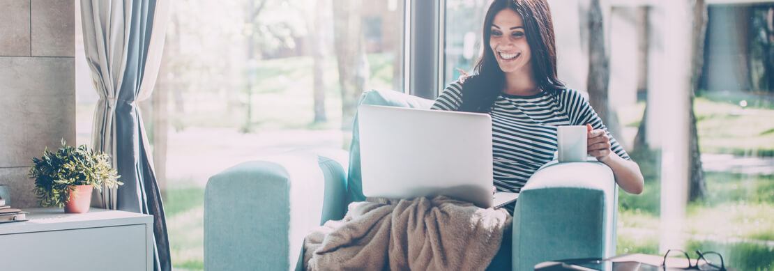 woman enjoying some time gaming on her laptop relaxing in an easy chair with coffee