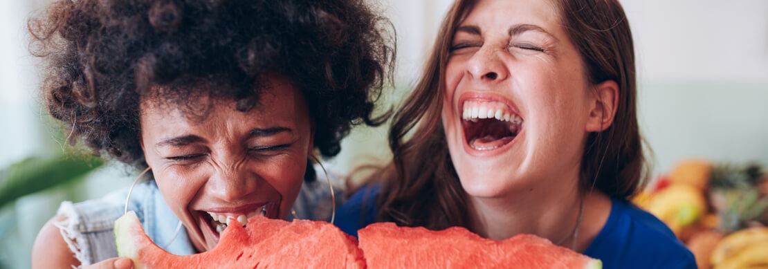 two woman eating watermelon and laughing out loud