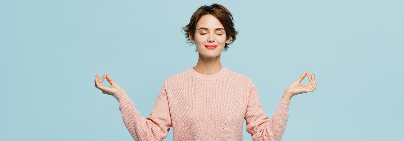 a woman calming herself with yoga. She is sitting with legs crossed, eyes closed, and a closed lips smile on her face