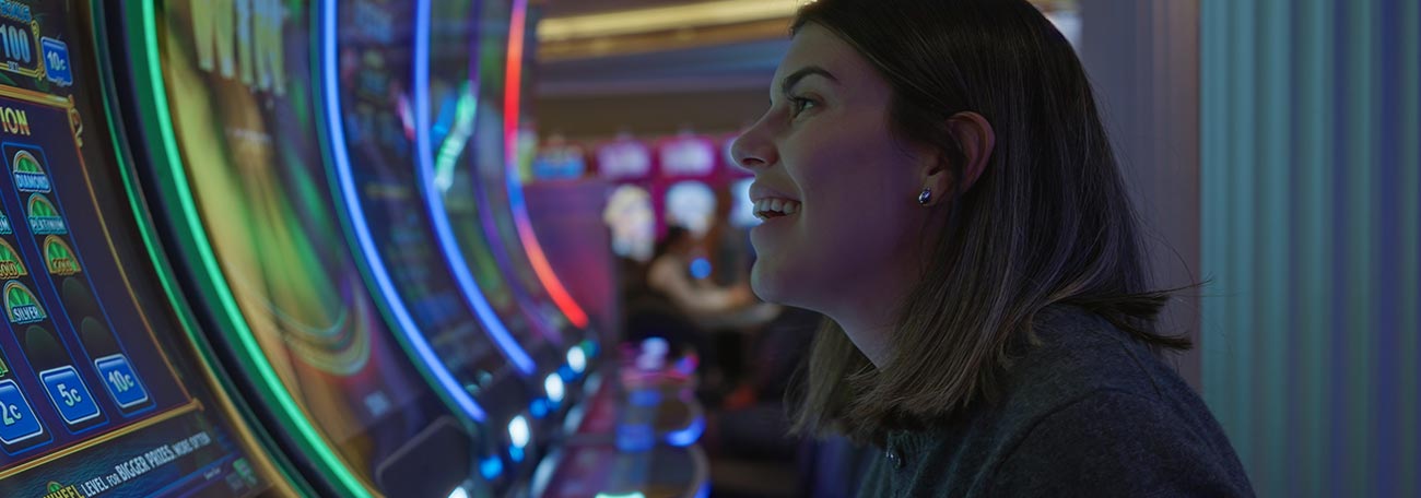 a thirty-ish woman smiling broadly at a slot machine in a land-based casino