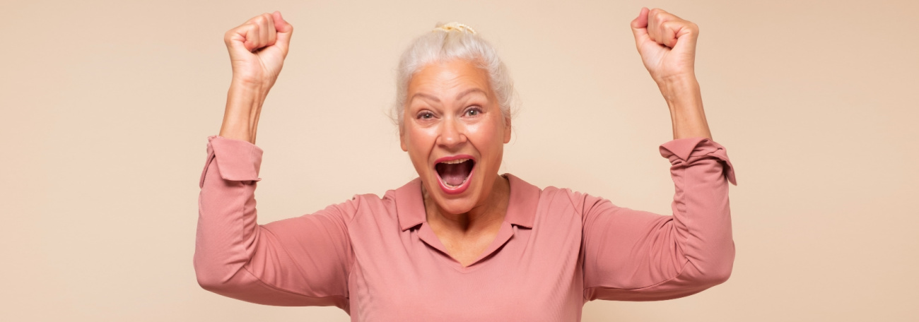 woman with short white hair wearing a pink top ecstatic about winning a jackpot