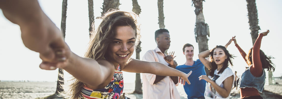 a group of handsome and happy young men and women on a beach with palm trees overhead