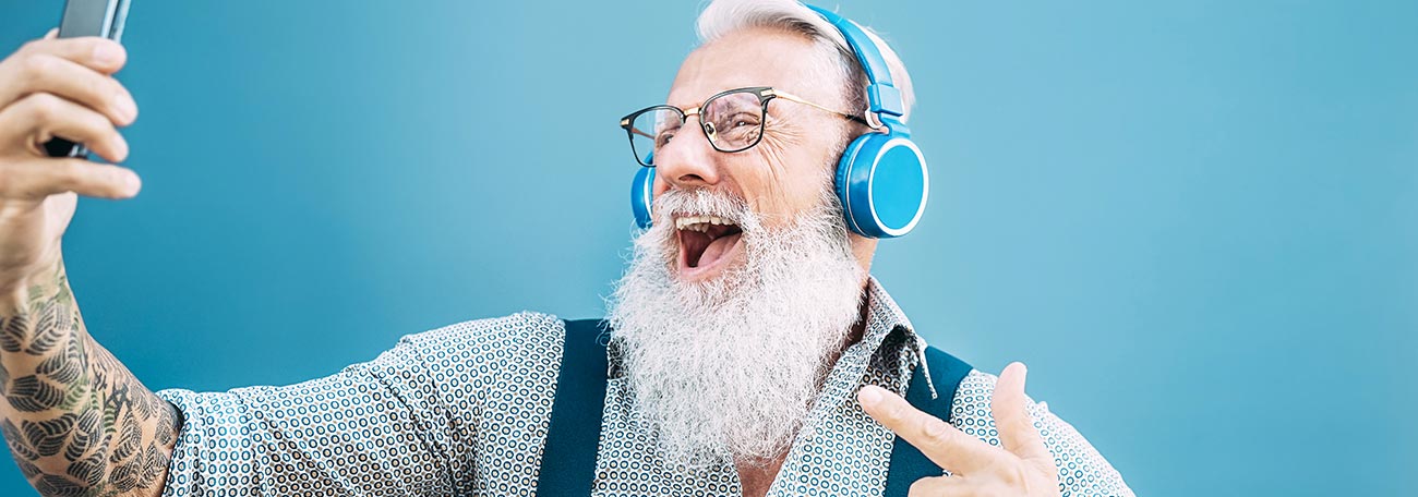 a man with a long white beard, suspenders, a headset, and tattoos on his arms having fun gaming on mobile